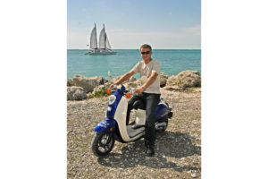 One guy on a one person blue and white scooter rental posing at Fort Zachary Taylor by the ocean with a sailboat in the background.